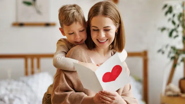 Chłopiec obejmuje mamę, która czyta kartkę z sercem. To piękna zagadka o mamie, pełna miłości.