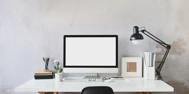 Nowoczesne biurko z monitorem, klawiaturą i lampką. Idealne miejsce do pracy zdalnej, gdzie pulpit zdalny pozwoli Ci połączyć się z biurem.