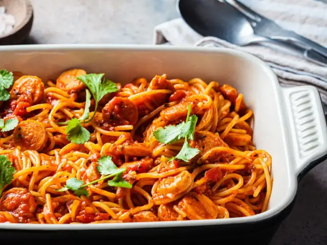 Pyszne spaghetti z kiełbasą w sosie pomidorowym, udekorowane kolendrą. Idealny pomysł, co zrobić z makaronem spaghetti na szybki obiad.