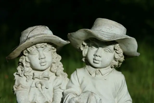 Zwei alte Gartenfiguren aus Stein, Kinder mit Hüten, im Grünen.