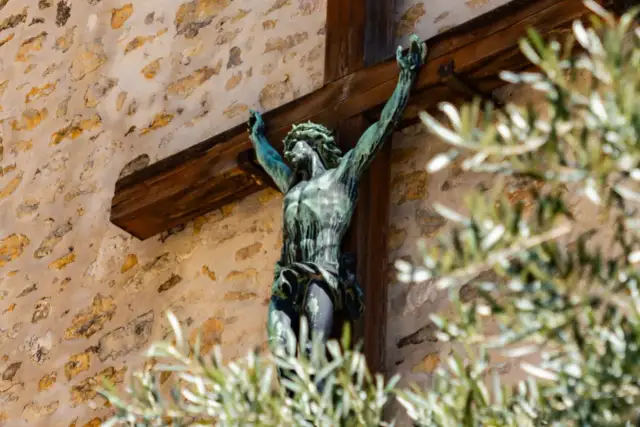 Brązowy Jezus na krzyżu, symbol chrześcijaństwa, na tle kamiennej ściany.
