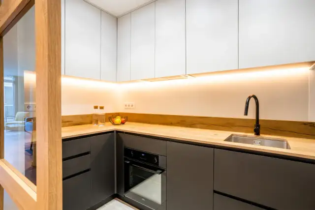 Cocinas negras y madera, con encimera de madera clara, armarios superiores blancos y detalles modernos.