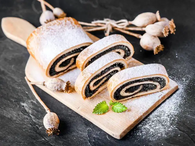 Stary przepis na makowiec, pyszny, zawinięty w ciasto i posypany cukrem pudrem. Obok suszone maki.