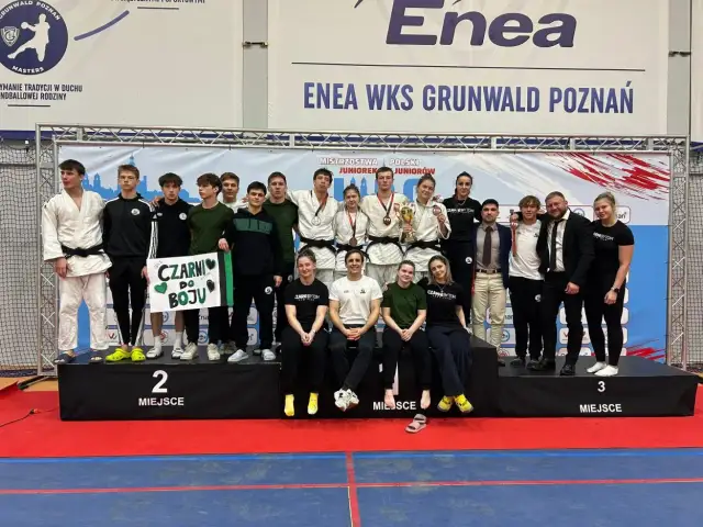 Młodzi sportowcy świętują sukces na mistrzostwa polski juniorów. Drużyna z transparentem "Czarni do boju" pozuje na podium.