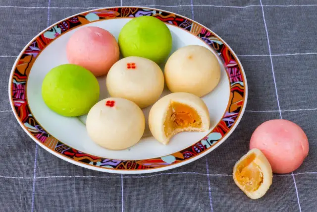 Kolorowe mochi z żółtym nadzieniem na talerzu z ozdobnym brzegiem.