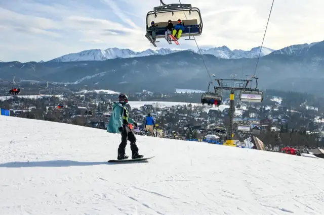 Snowboardzista na stoku, w tle kolejka krzesełkowa i góry. Zastanawiasz się, ile kosztuje karnet na narty?