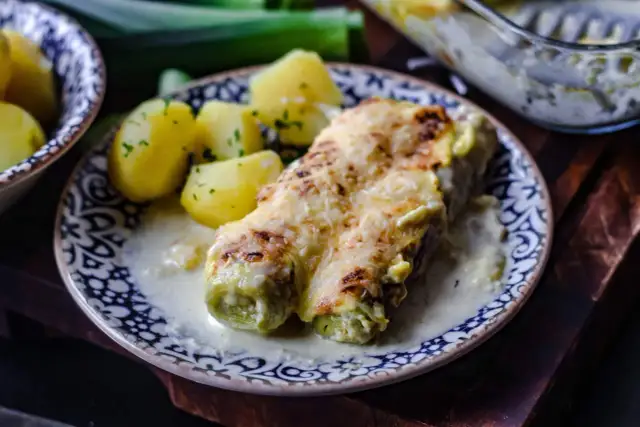 Gebackener Lauch mit Schinken, überbacken mit Käse, serviert mit Salzkartoffeln und einer cremigen Sauce.