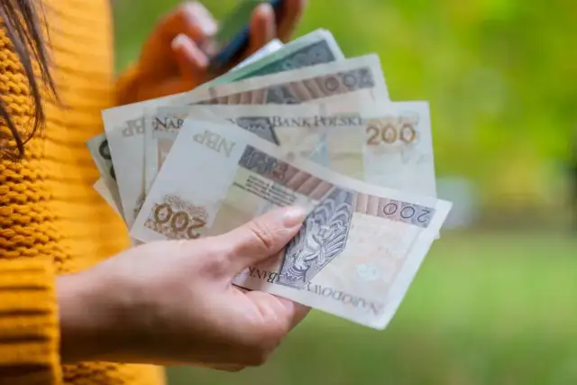 Dłoń trzyma polskie banknoty 200 zł. To może być dodatek wyrównawczy, który pomoże w codziennych wydatkach.