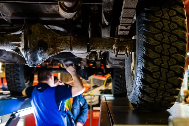 Mechanik sprawdza podwozie terenowego auta z napędem **awd**. Widoczna jest masywna oś i bieżnik opony.