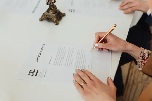 Kobieta podpisuje dokument "DIVORCE DECREE". Wniosek o rozwód można pobrać online.