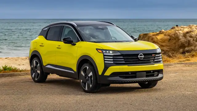 Żółty Nissan Kicks z czarnym dachem stoi na plaży przy spokojnym morzu.