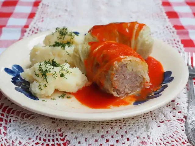 Gołąbki z kapusty włoskiej, podane z purée ziemniaczanym i polane sosem pomidorowym, ozdobione koperkiem.