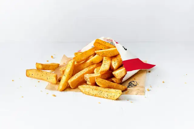 Stos małych frytek z KFC wysypany z papierowej torebki na białym tle.