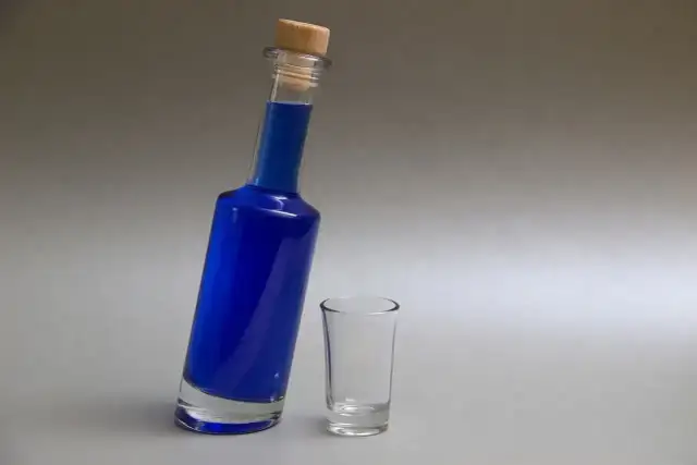 Niebieska wódka w butelce z korkiem i pusty kieliszek obok.