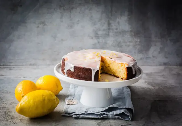 Ein saftiger zitronenkuchen mit Zuckerguss und Zitronenschale, daneben frische Zitronen.