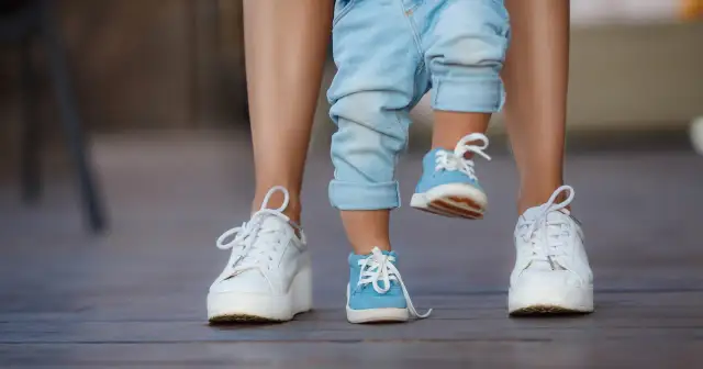 Dziecko w niebieskich bucikach i dorosły w białych sneakersach na drewnianej podłodze.