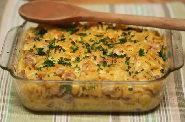 Zapiekanka makaronowa z boczkiem i serem, posypana natką pietruszki, w szklanym naczyniu.