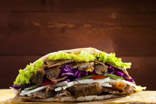 Duży kebab z mięsem, sałatą, czerwoną kapustą i warzywami.