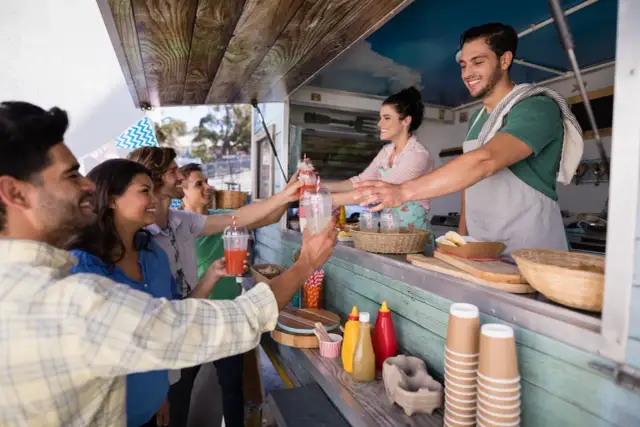 Uśmiechnięci ludzie odbierają napoje od barmanów z food trucka.