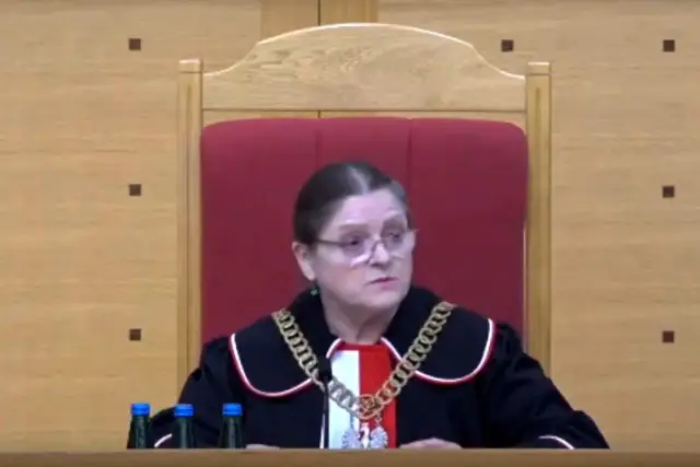 Sędzia w todze i łańcuchu na szyi, siedzi za stołem z butelkami wody. Czy sędziowie płacą składkę zdrowotną?