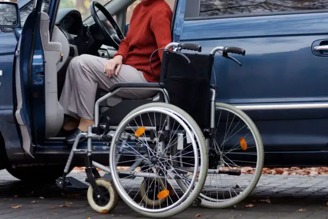 Osoba w wózku inwalidzkim obok otwartych drzwi samochodu. Wózek jest gotowy do podróży, zapewniając ulgę na samochód i mobilność.