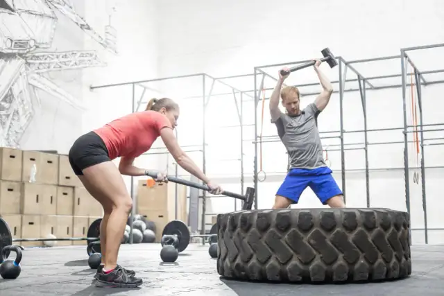 Kobieta i mężczyzna ćwiczą z młotami na oponie w siłowni CrossFit.
