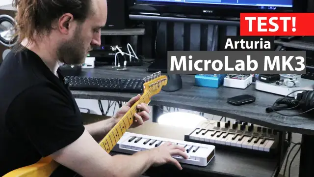 Mężczyzna gra na gitarze, obok niego leży biały midi keyboard Arturia MicroLab MK3.