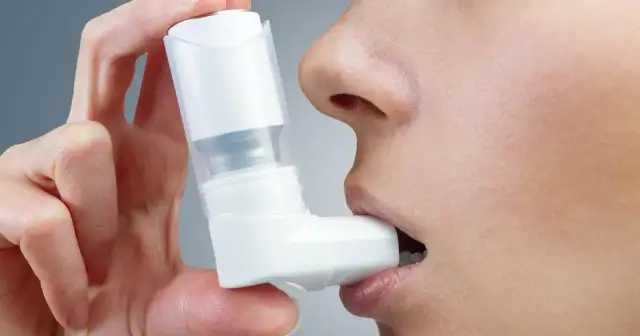 Dłoń trzymająca inhalator przy ustach osoby.