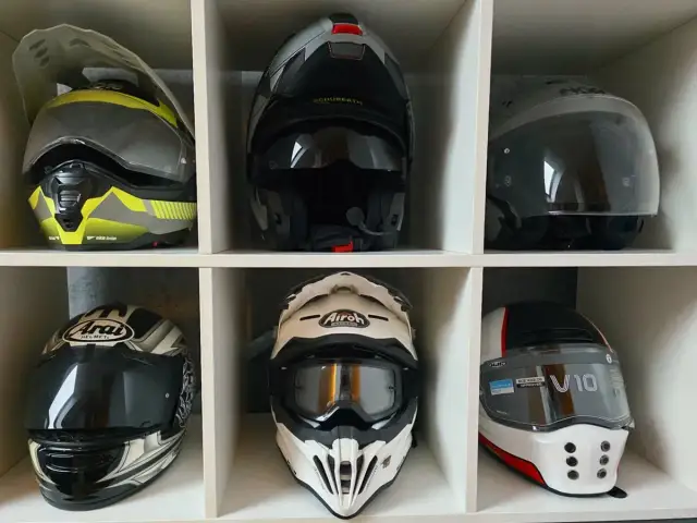 Sześć kasków motocyklowych w różnych kolorach i stylach, ułożonych w sześciu przegrodach.
