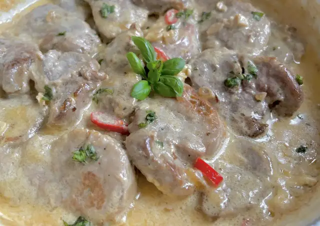 Soczyste polędwiczki w kremowym sosie camembert, udekorowane listkami bazylii i kawałkami papryki. Pyszne danie gotowe do podania.