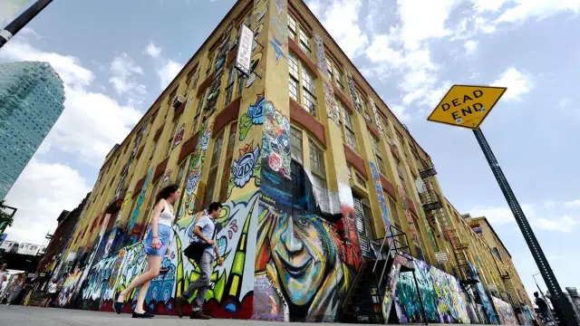 Gelbes Gebäude mit Graffiti-Kunst, Menschen gehen vorbei, "DEAD END"-Schild.