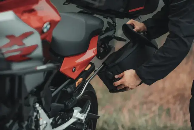 Mężczyzna montuje czarną sakwę motocyklową do czerwonego motocykla.