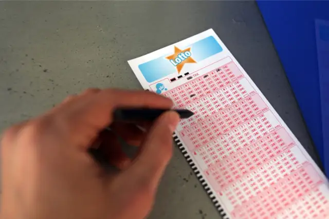 Ręka z długopisem zaznacza liczby na kuponie Duży Lotek. Dowiedz się, jak wypełnić kupon lotto duży lotek i spróbuj szczęścia!