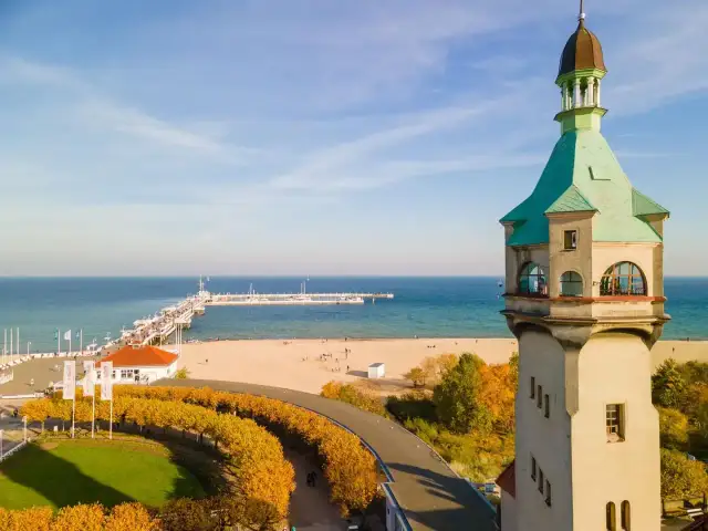 Widok na latarnię morską w Sopocie, plażę i molo w jesienny, słoneczny dzień.