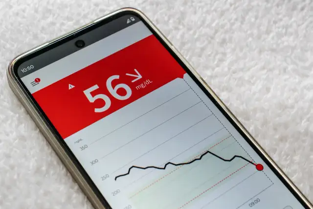 Niski poziom glukozy 56 mg/dL na ekranie telefonu, wskazujący na hipoglikemię reaktywną. Wykres pokazuje gwałtowny spadek.
