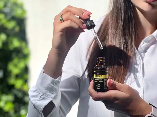 Kobieta trzyma buteleczkę z olejkiem Sattva i pipetkę z serum do włosów.