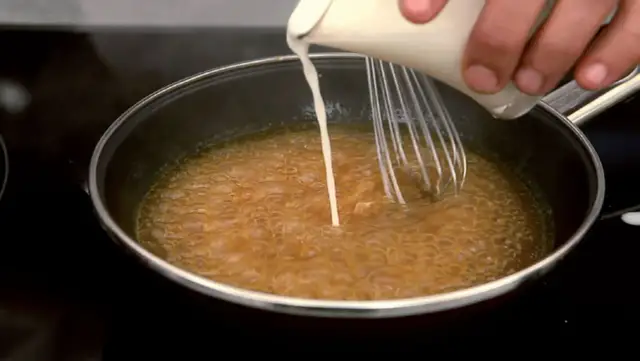 Se añade líquido a una sartén con salsa burbujeante, usando un batidor para espesar salsa con maicena.
