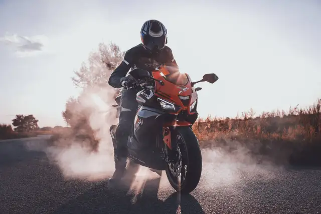 Motocyklista w kasku i kombinezonie na pomarańczowym Barton Blade 125, z którego wydobywa się dym. Zastanawiasz się, ile pali motor 125?