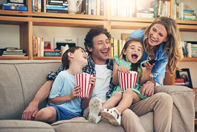 Rodzina śmieje się do rozpuku, jedząc popcorn podczas oglądania filmu dla całej rodziny.