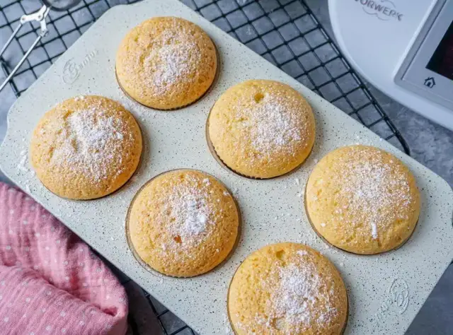 Sechs goldbraune Muffins, mit Puderzucker bestäubt, auf einer hellen Backform. Perfekt für den Thermomix!