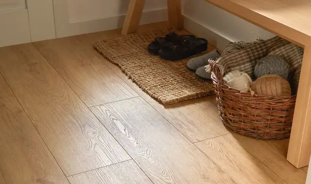 Jasna podłoga w przedpokoju w bloku, z dywanikiem, klapkami i koszem z włóczkami pod ławką.