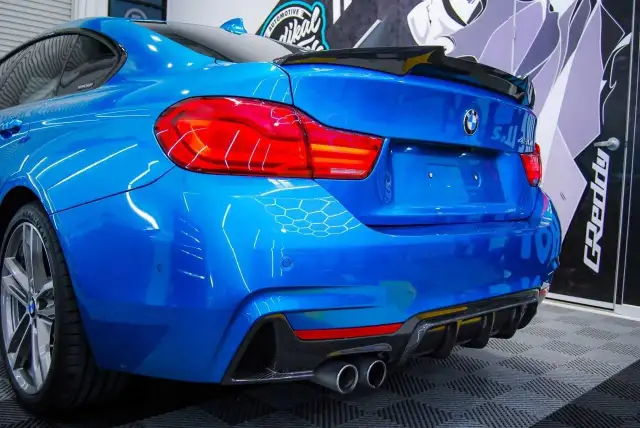 Niebieskie BMW z czarnym spoilerem na klapie bagażnika i dyfuzorem z włókna węglowego.