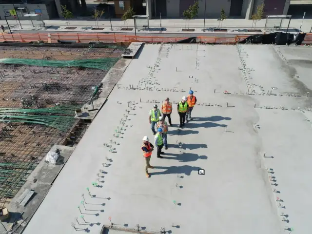 Ekipa budowlana na placu budowy, dyskutująca o tym, ile kosztuje metr sześcienny betonu. Widać zbrojenie i świeżo wylany beton.