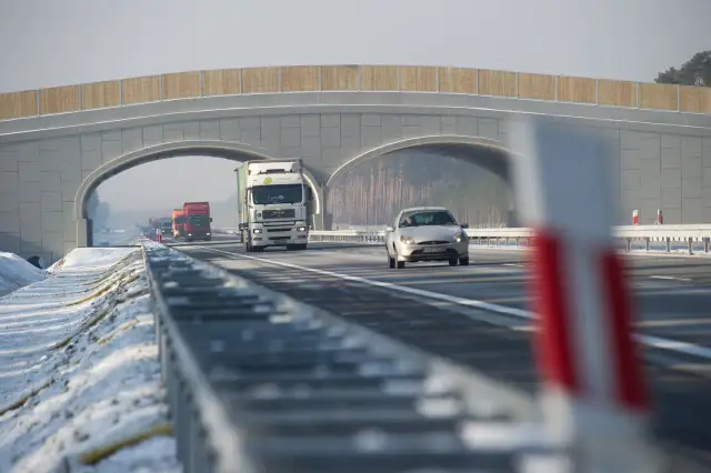 Autostrada A2 z mostem nad jezdnią, jadące samochody i ciężarówki w zimowej scenerii.