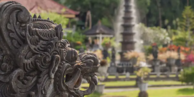 Eine detaillierte Steinskulptur eines Fabelwesens im Vordergrund, im Hintergrund ein Garten mit Brunnen und Pflanzen.