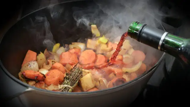 Verduras cocinándose en una olla, se vierte vino tinto. El vapor sube, indicando que el alcohol se evapora rápido.