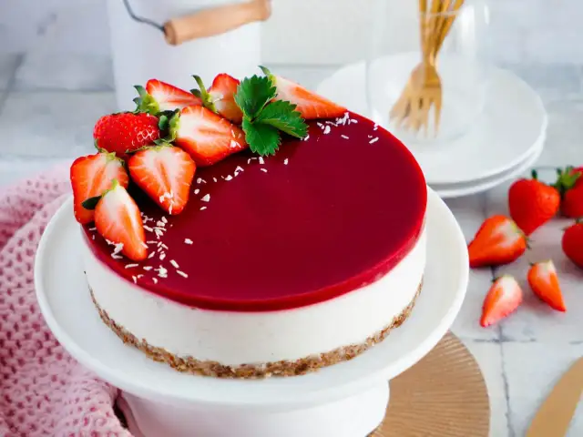 Ein köstlicher veganer Cheesecake ohne Backen, dekoriert mit frischen Erdbeeren und einem glänzenden Fruchtspiegel.