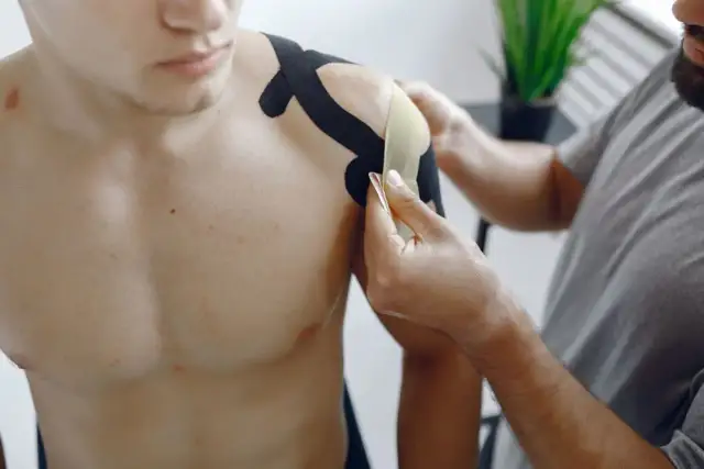 Fizjoterapeuta okleja taśmą bark mężczyzny, łagodząc ból barku po laparoskopii.