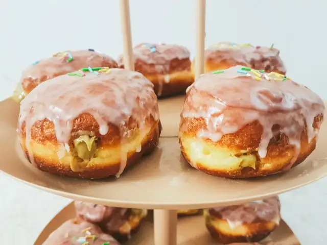 Pyszne pączki pistacjowe z lukrem i kolorową posypką, ułożone na paterze.