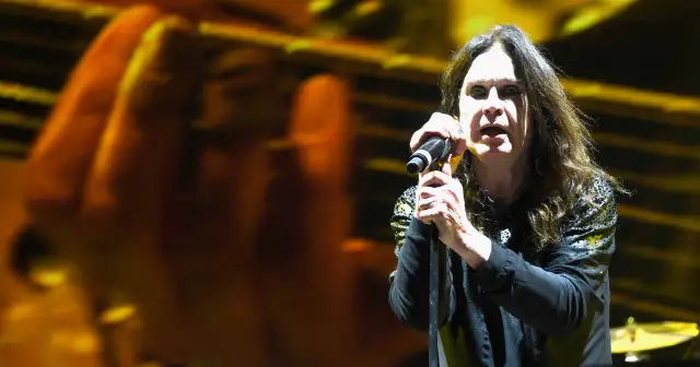 Ozzy Osbourne śpiewa do mikrofonu na koncercie, z rozmytym tłem w kolorach żółci i pomarańczy.